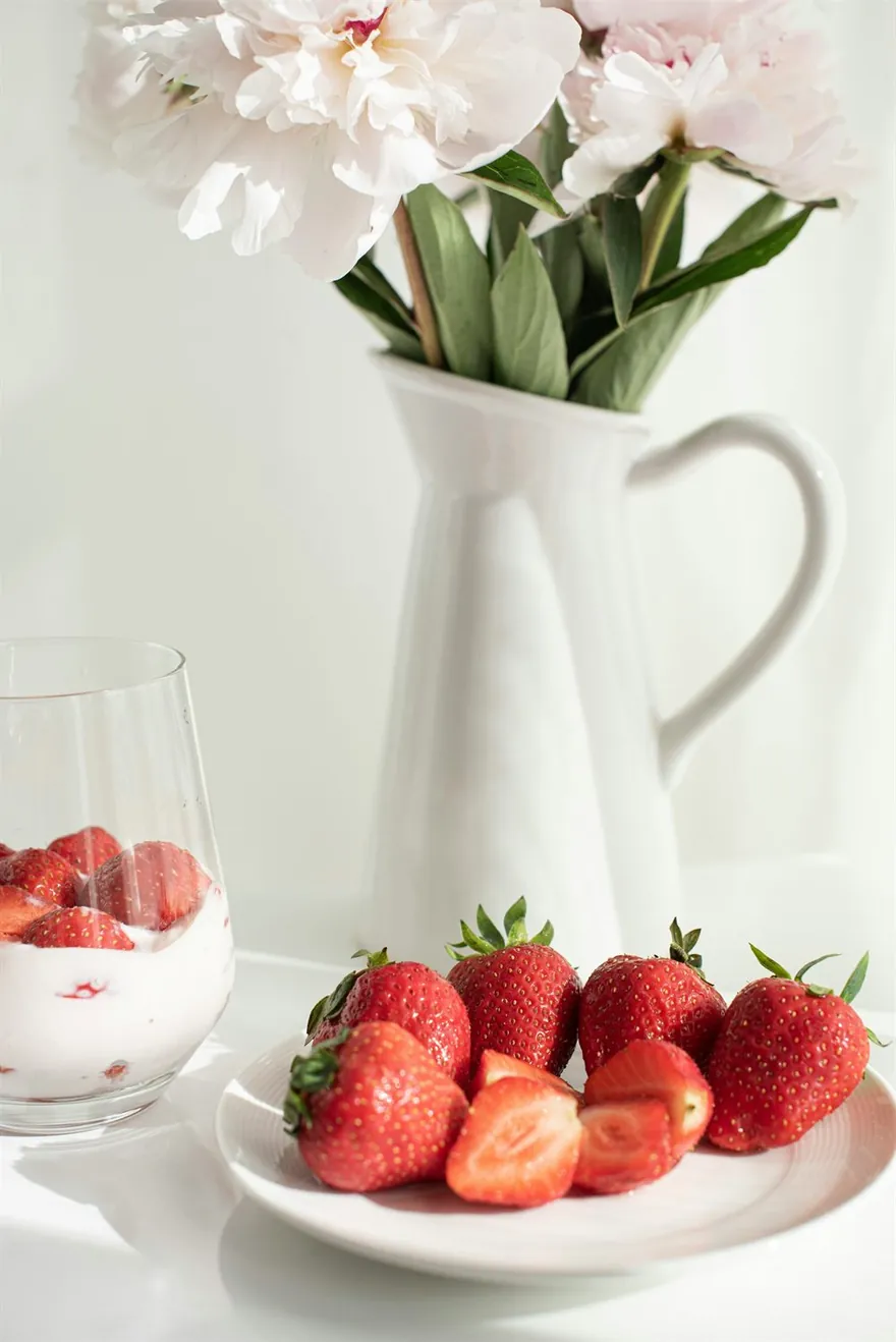 Plate of strawberries, a glass of strawberries and cream, and a white vase of flowers