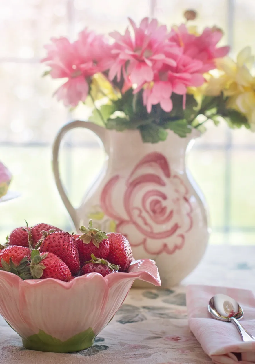 Bowl of strawberries and a jug of flowers on a sunny table